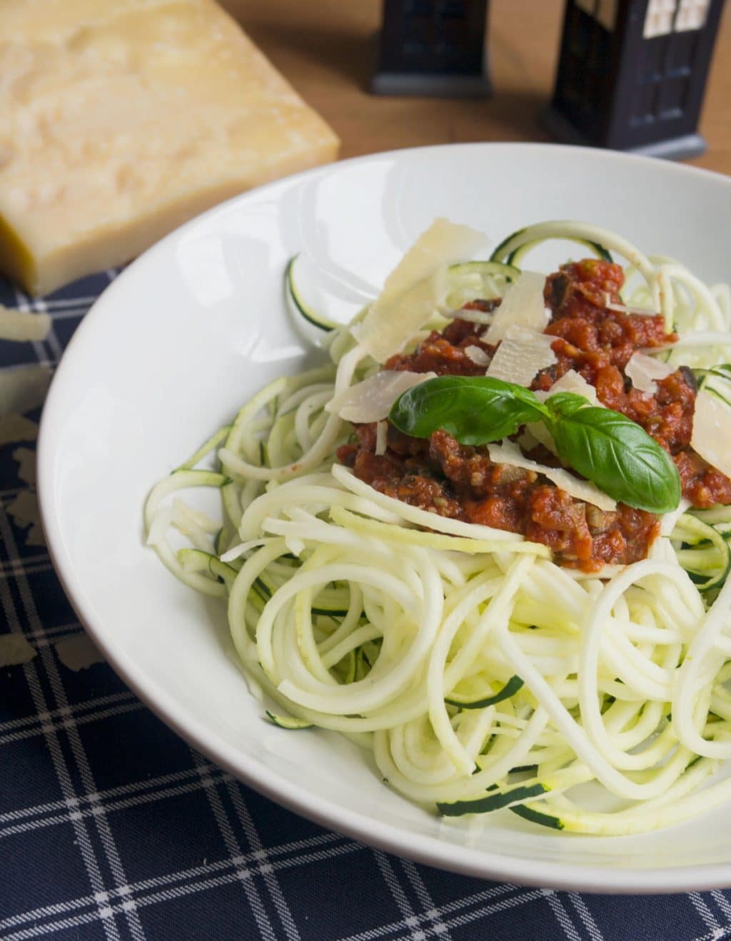 Zucchini Spaghetti mit Puttanesca Sauce und Parmesan auf weißem Teller