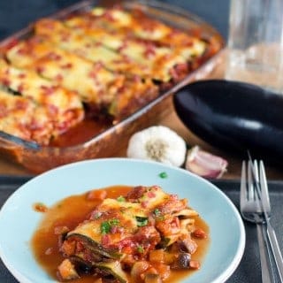 Zucchini Lasagne auf einem hellblauen Teller mit Auflaufform im Hintergrund