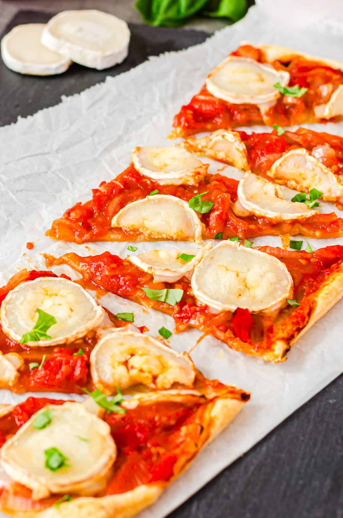 Blätterteigtarte mit geschmorten Tomaten und Ziegenkäse auf weißem Backpapier