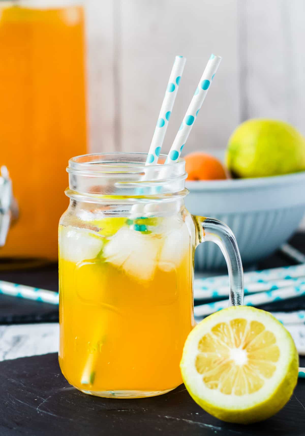 Ein Glas mit Aprikosenlimonade und Eis mit halber Zitrone im Vordergrund