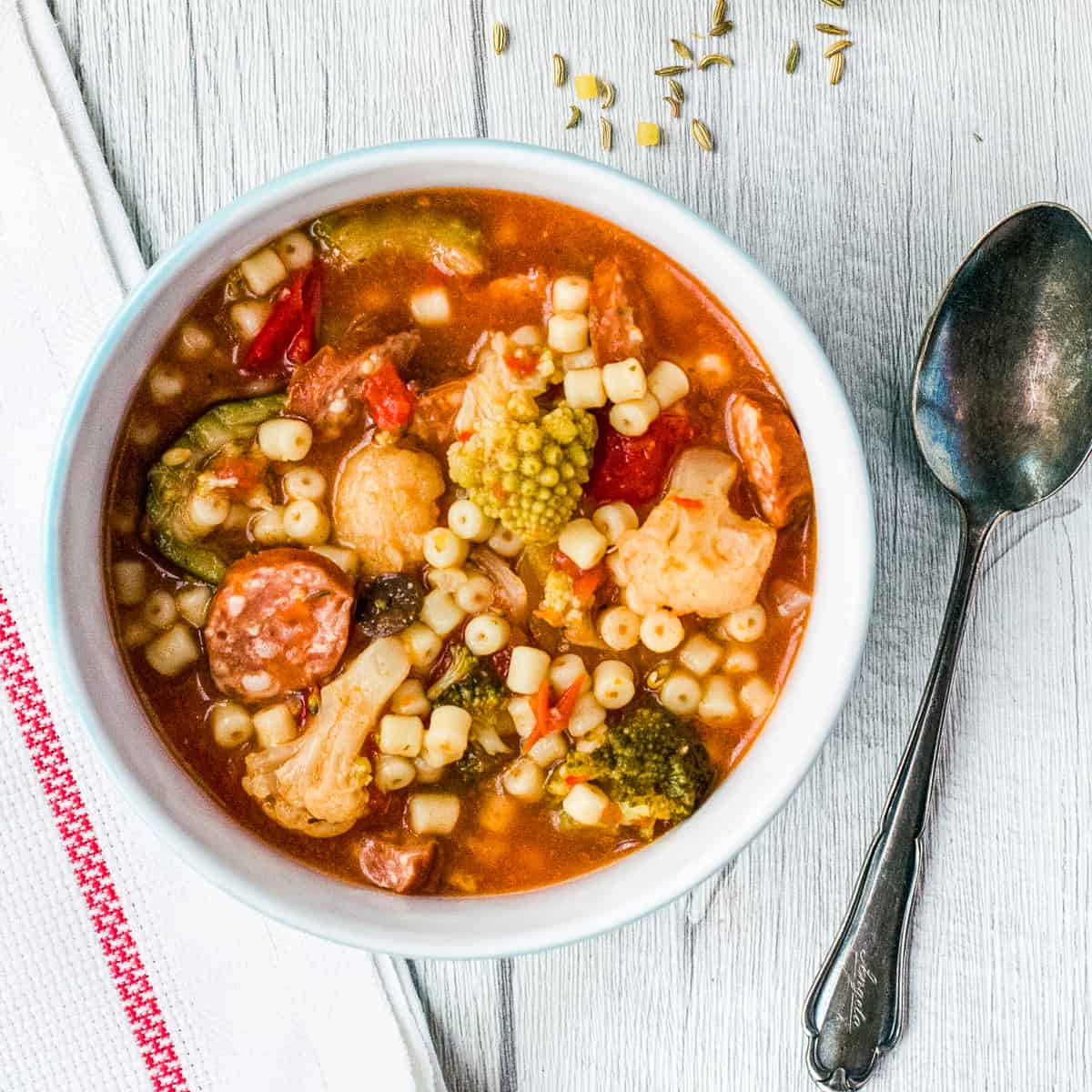 Gemüsesuppe mit Nudeln in weißer Schale mit Löffel daneben von oben