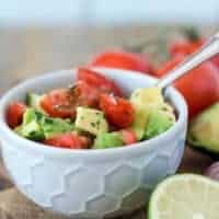 Tomaten-Avocado-Salat in einer hellgrauen Schüssel mit Limette dekoriert