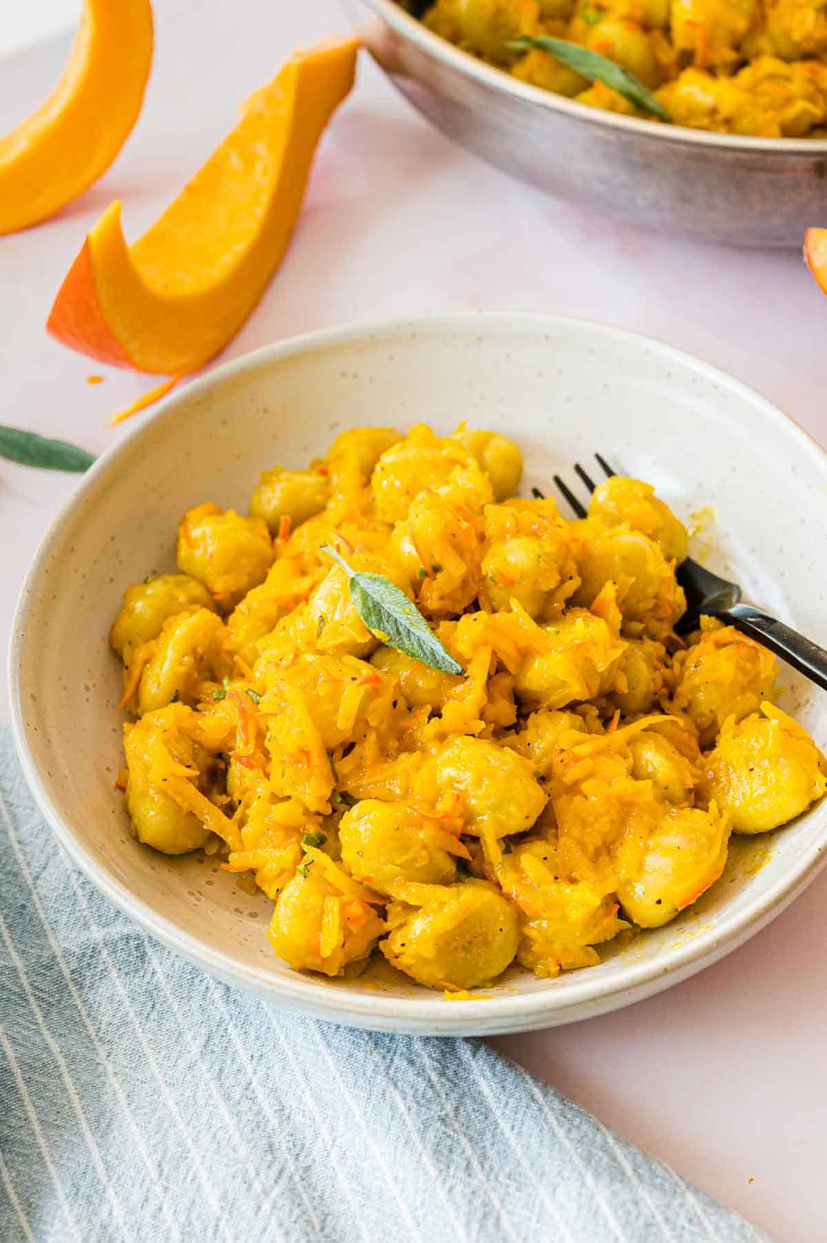 Gnocchi mit Kürbis und Salbeiblatt in heller Schale mit schwarzer Gabel