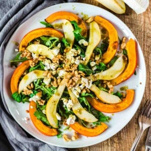 Herbstsalat mit Birnen- und Kürbisspalten auf weißem runden Teller von oben