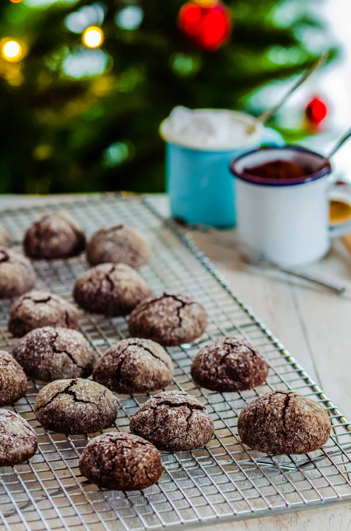 Schoko-Crinkle-Cookies mit Puderzucker auf Kuchengitter mit Weihnachtsbaum im Hintergrund
