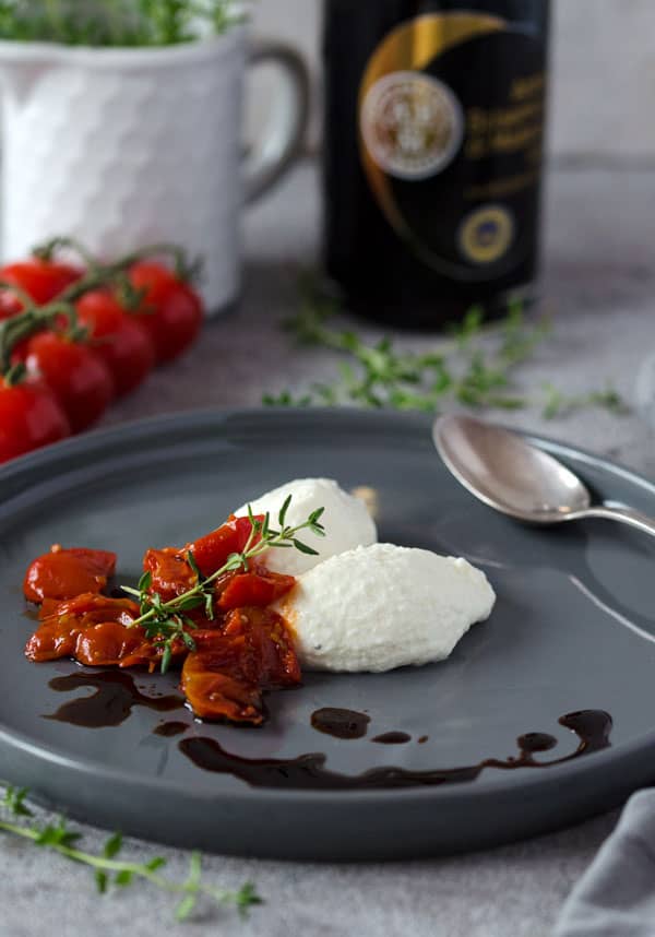 Panna Cotta Nocken mit gerösteten Tomaten getoppt auf grauem Teller