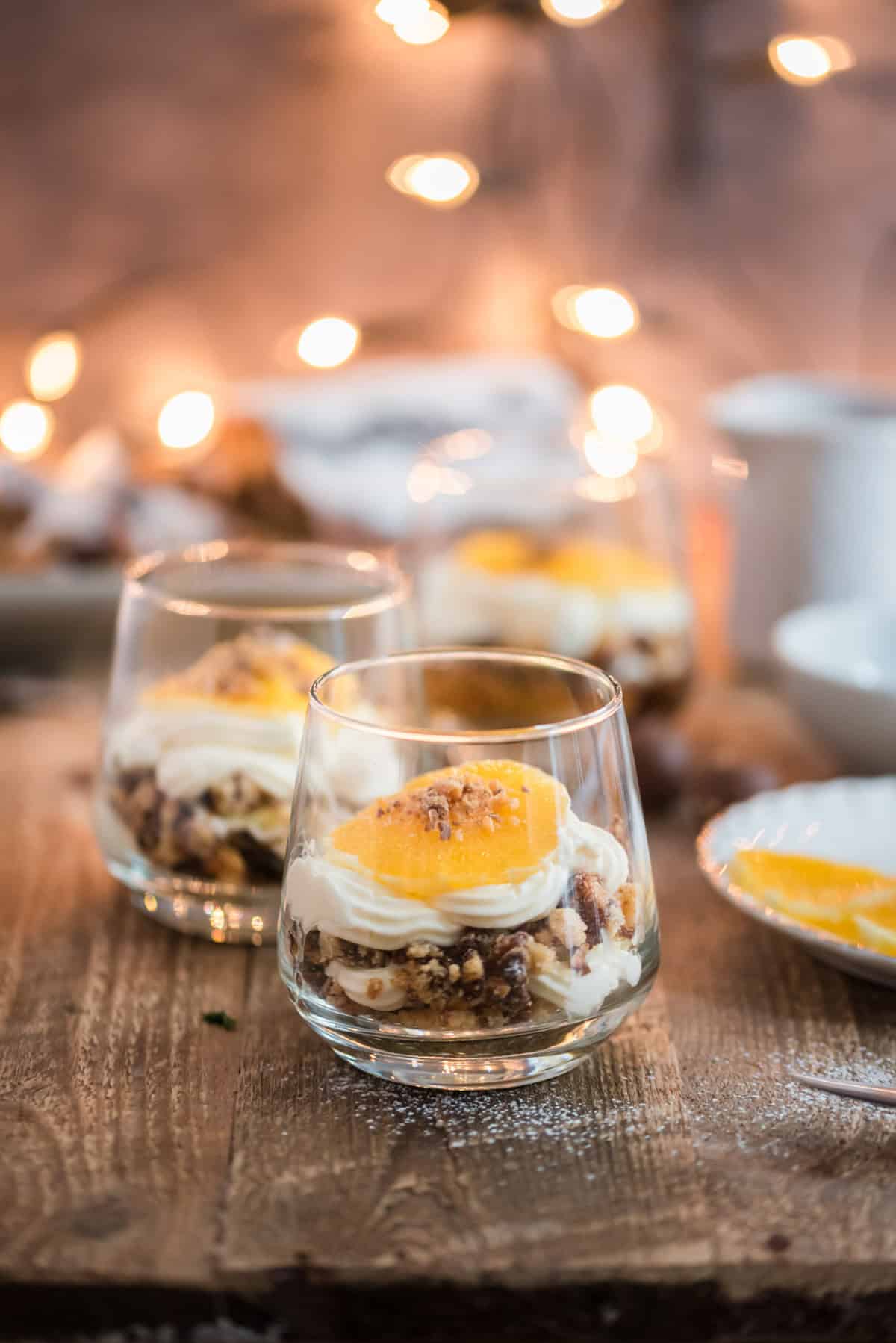 Mehrere Gläser mit Schichtdesser auf Holztisch, mit Lichtern im Hintergrund