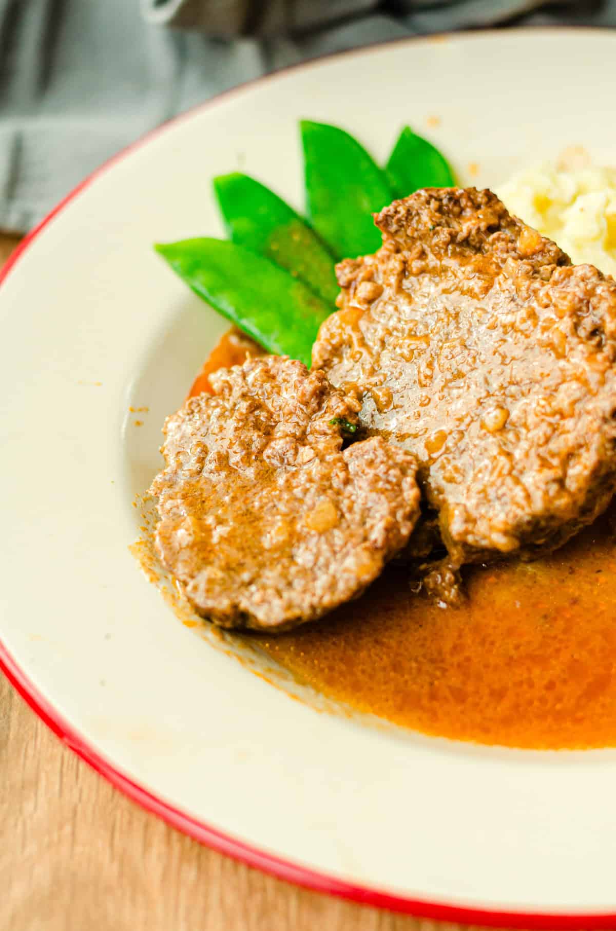 zwei Scheiben Hackbraten mit Sauce, Kartoffelpüree und Zuckerschoten auf einem Teller