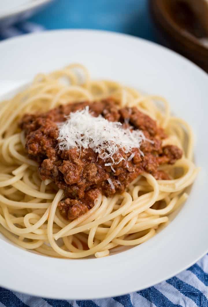 Spagetti Bolognese mit geriebenem Parmesan auf einem weißen Teller mit Rand, Nachaufnahme