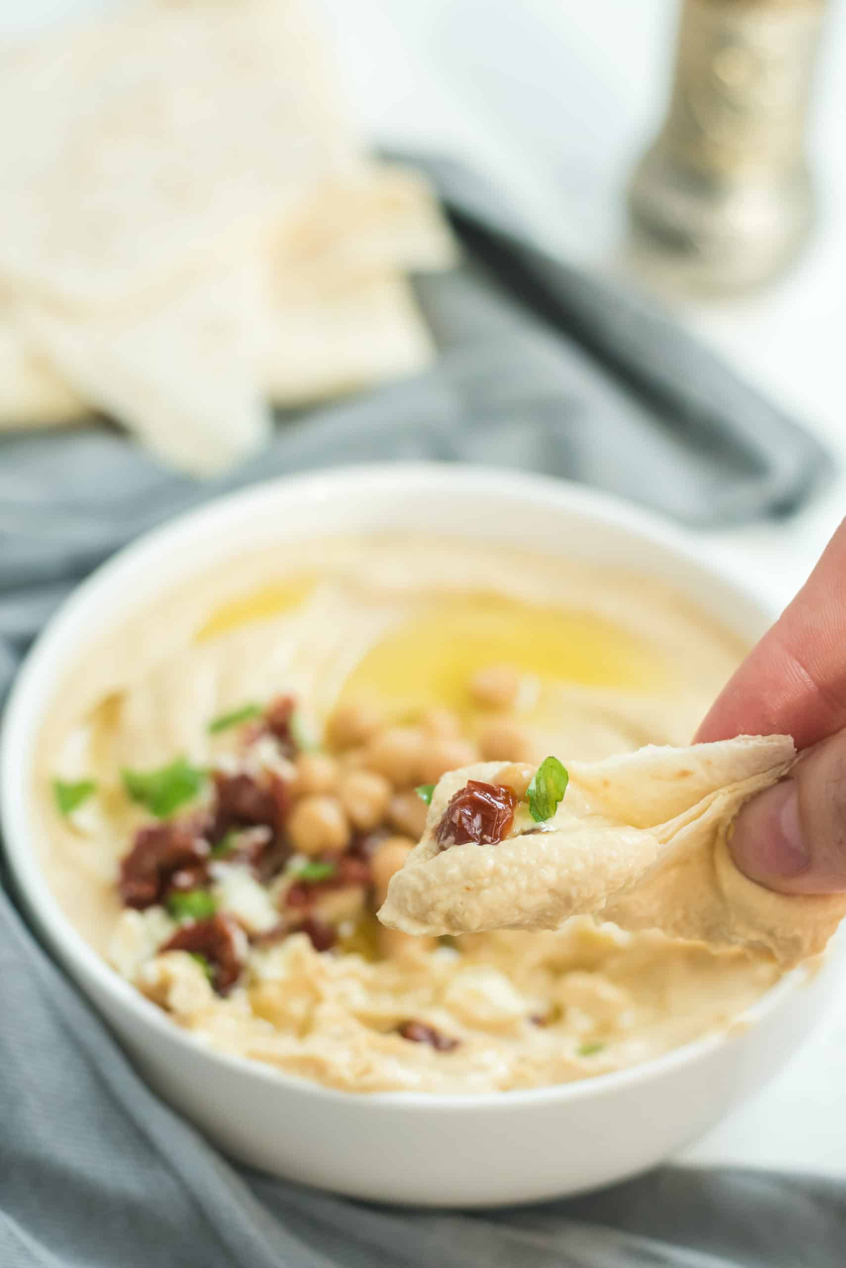 Hummus in einer weißen Schale, Hand mit Pitabrot und Hummus