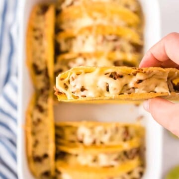 überbackene Tacos in weißer Auflaufform, einer in Hand