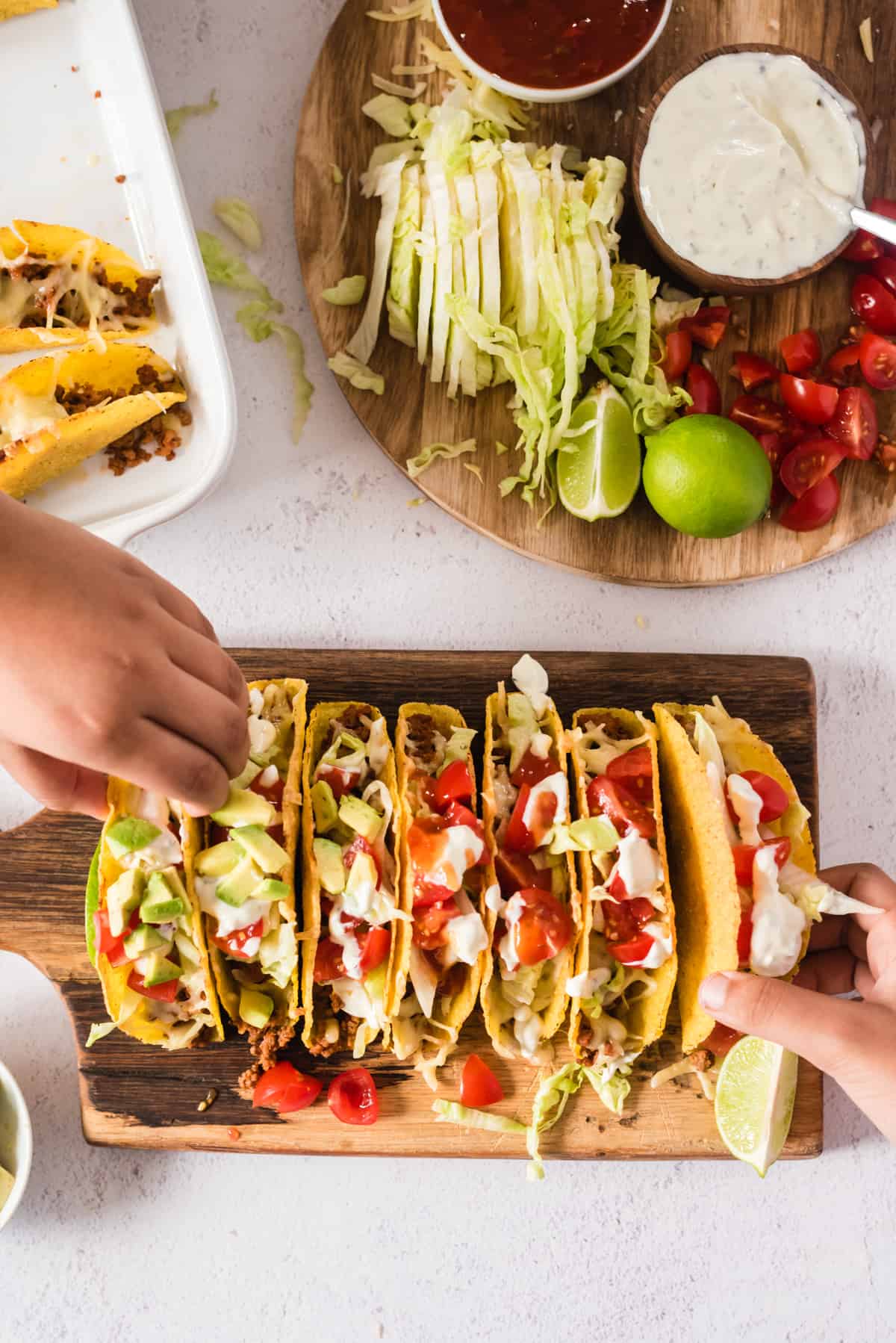 7 überbackene Tacos auf einem Holzbrett, zwei Hände nehmen sich je einen