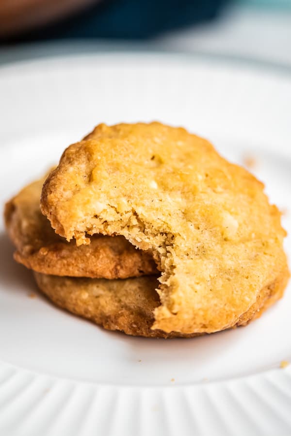 drei Macadamia Cookies mit weißer Schokolade auf einem weißen Teller, der oberste Keks angebissen
