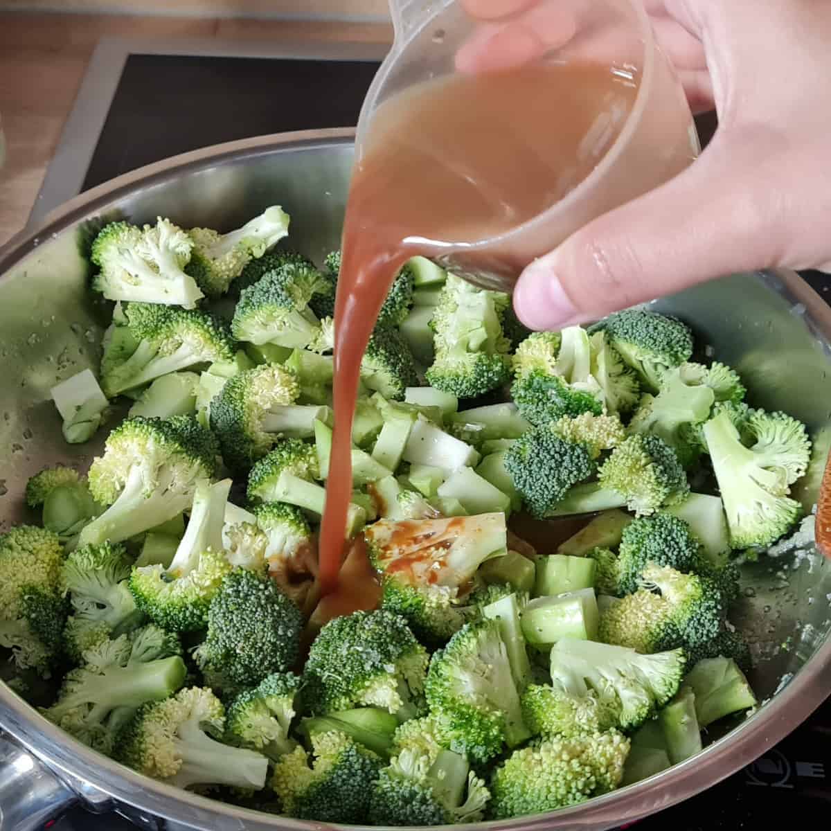 Soja-Sesamöl-Sauce wird über Brokkoli in Edelstahlpfanne gegossen