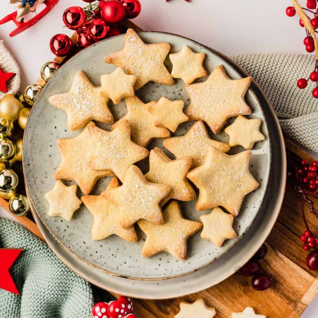 Butterplätzchen in Sternform auf einem hellen Teller mit Weihnachtsdeko drumherum von oben