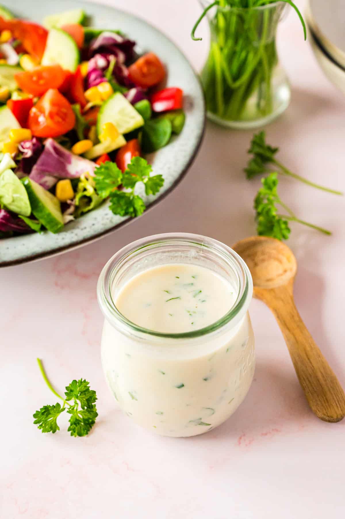 Joghurtdressing in Wecklglas mit Salat im Hintergrund