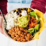 Mexikanische Reisbowl in einer hellen Schale von zwei Händen gehalten