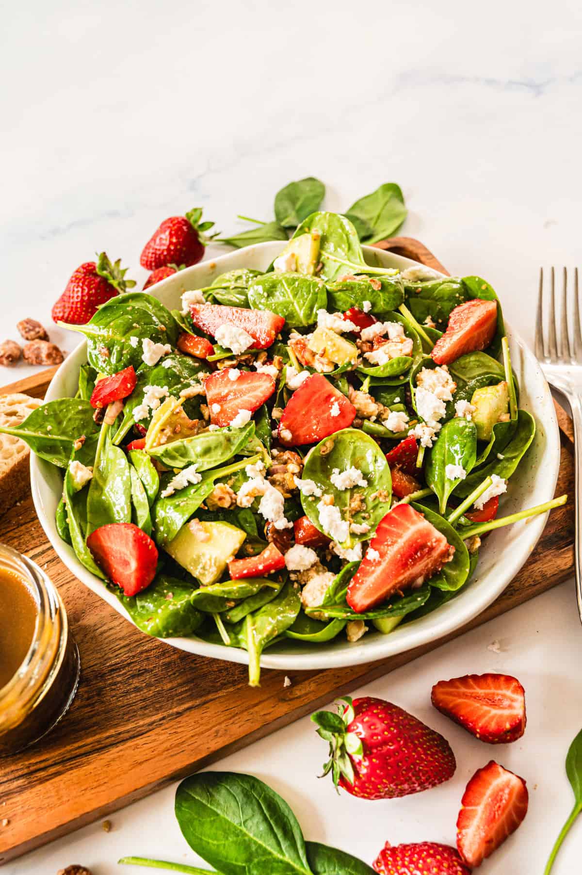 Spinatsalat mit Erdbeeren und Feta in weißer Schale auf Holztablett