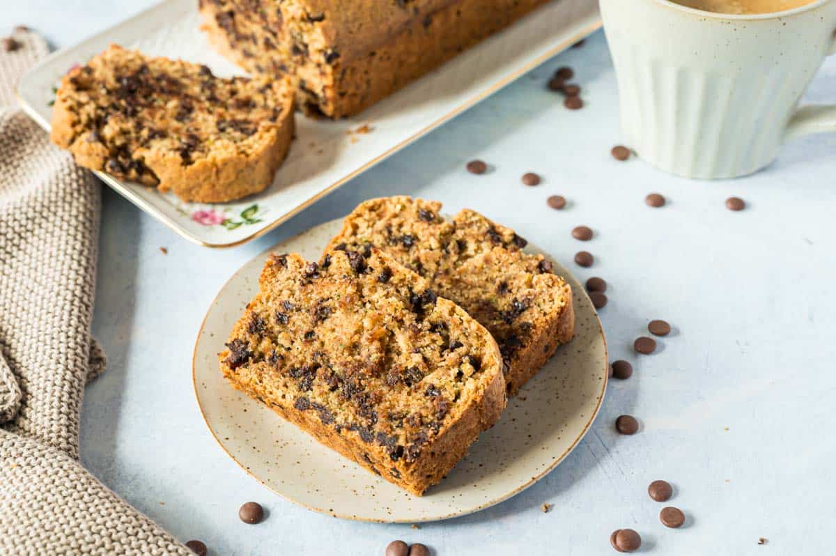 Zwei Stücke Zucchinikuchen auf kleinem hellen Teller, angeschnittener Kuchen dahinter