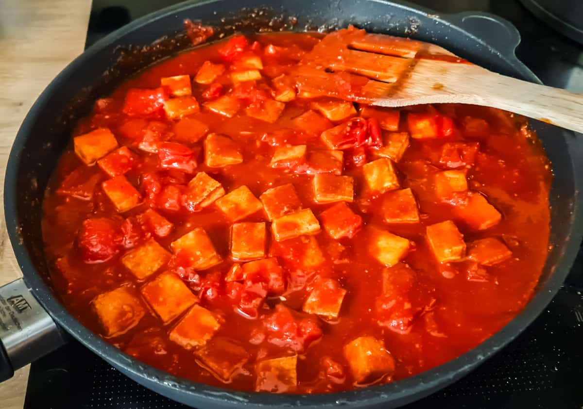 Gochujang Sauce und Tofu vermischt in schwarzer Pfanne mit Holzlöffel