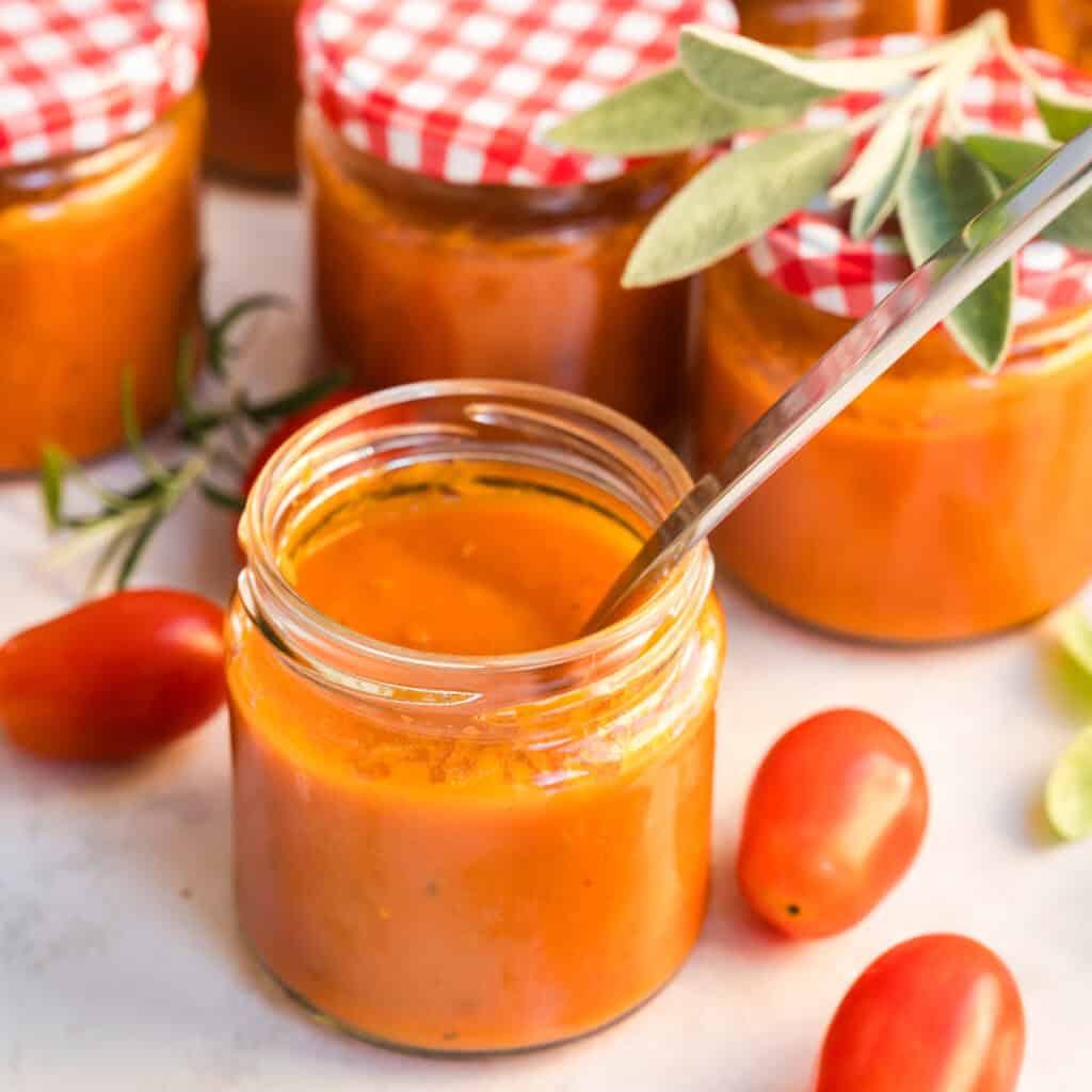 Mehrere Gläser mit Tomatensauce aus gebackenen Tomaten, eins offen und mit Löffel