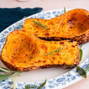 zwei gebackene Butternut Kürbis Hälften auf weißer Servierplatte mit blauem Blumenmuster am Rand