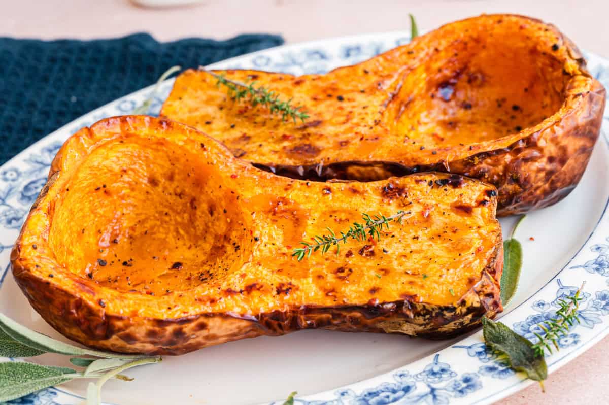 zwei gebackene Butternut Kürbis Hälften auf weißer Servierplatte mit blauem Blumenmuster am Rand