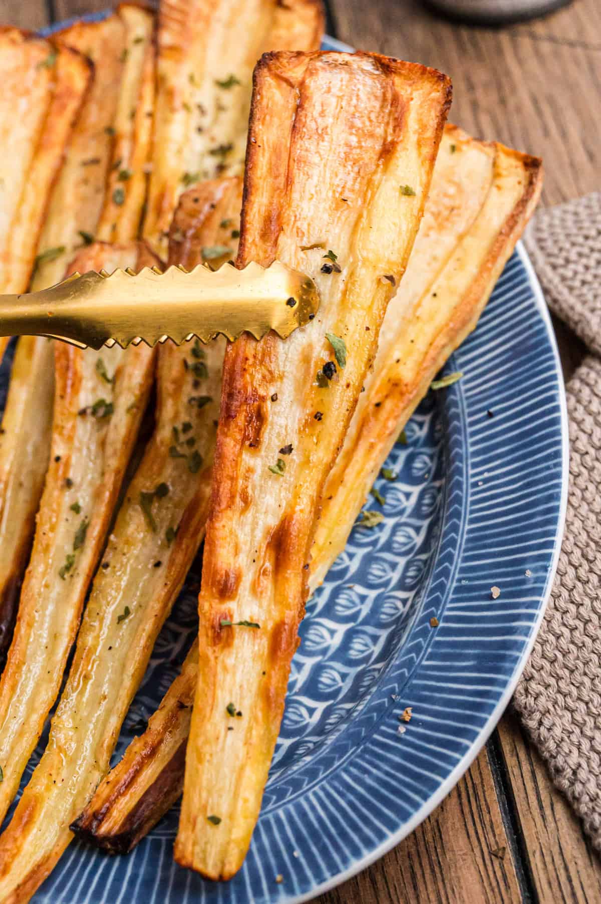 Gebackene Pastinake wird von goldfarbener Zange hochgehalten