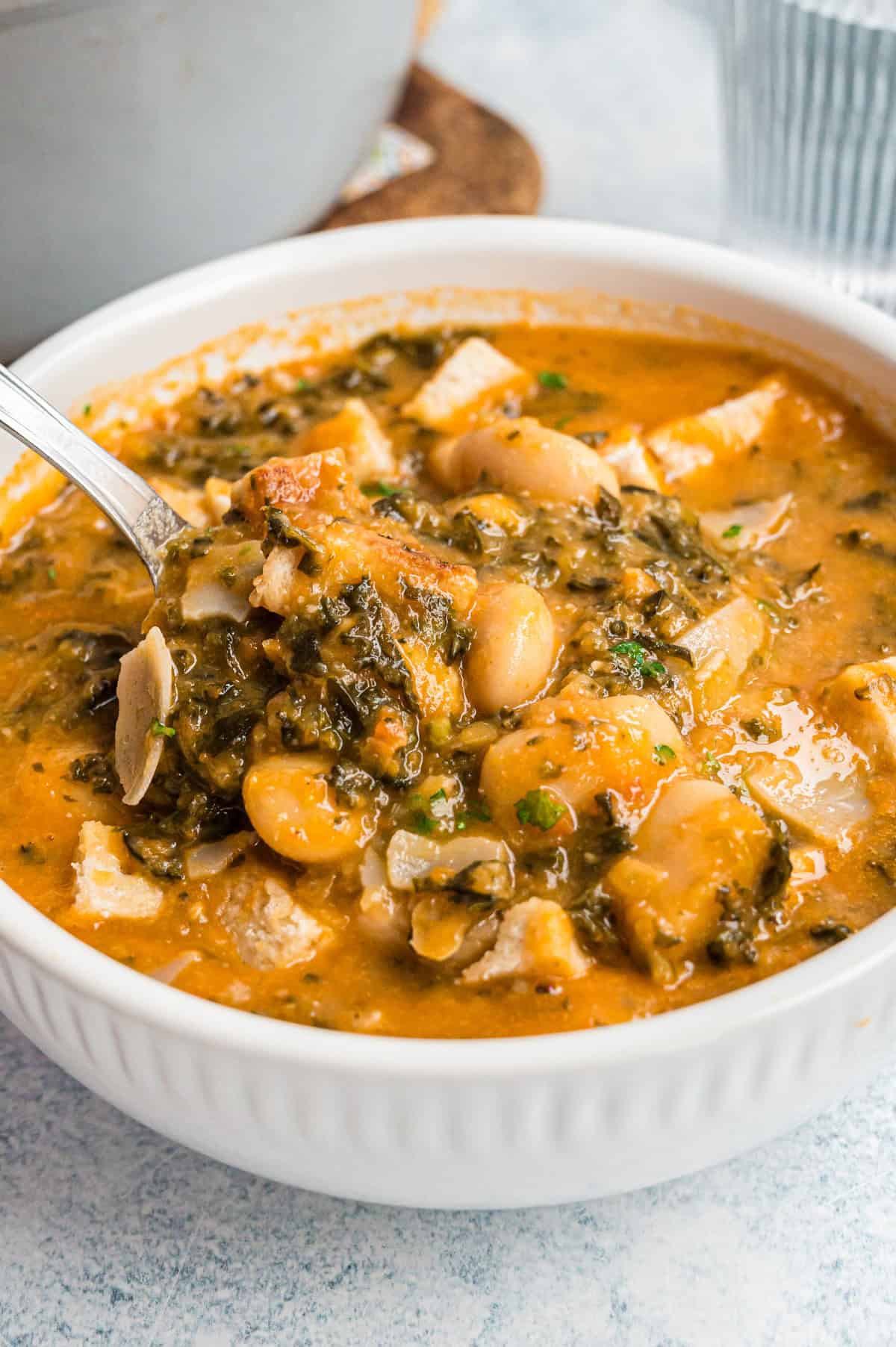 Ribollita mit veganem Parmesan und Petersilie in weißer Schale, Nahaufnahme mit Löffel