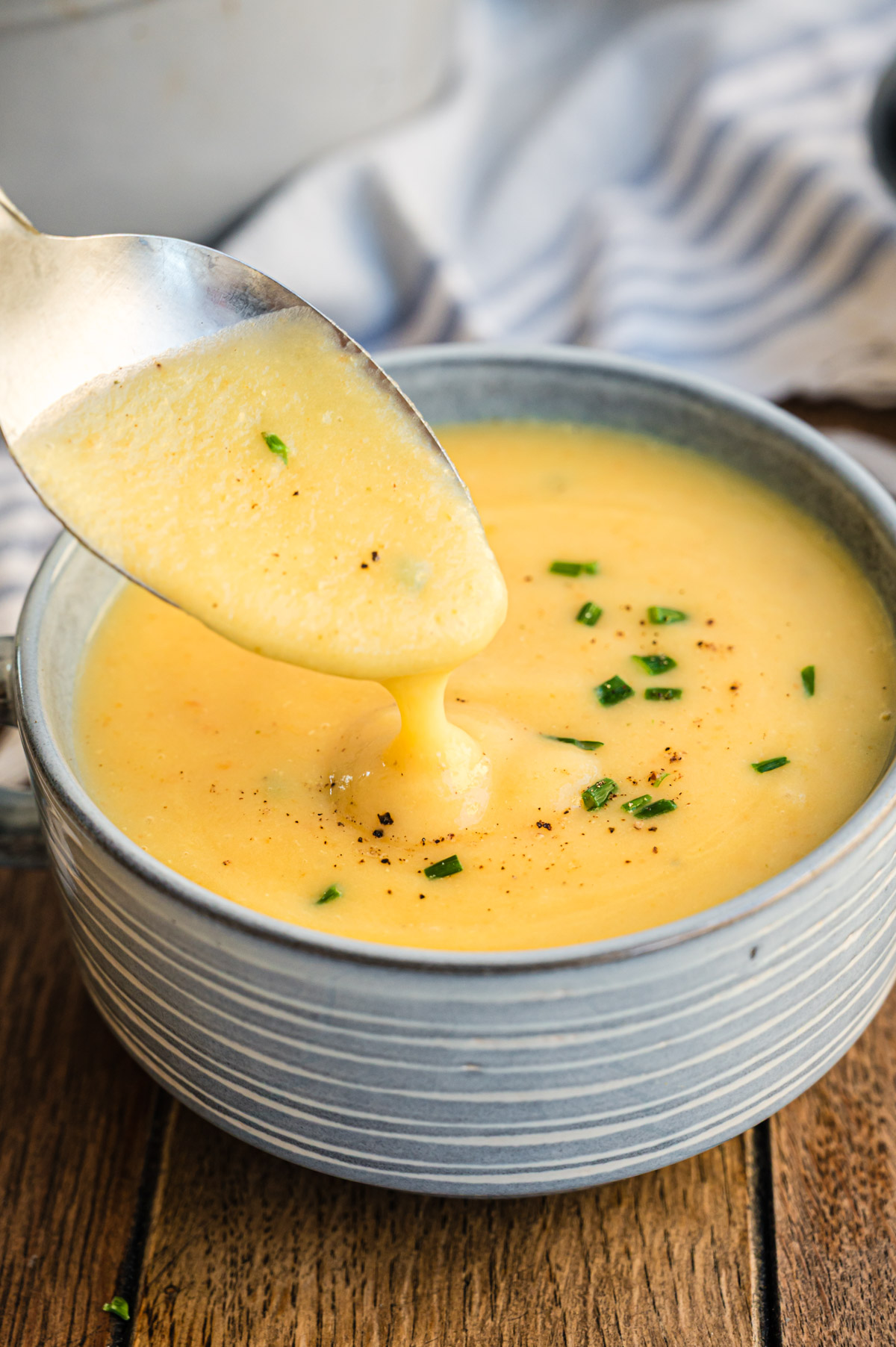 Kartoffelsuppe in blauer Suppenschale, Löffel darüber und Suppe läuft in die Schale