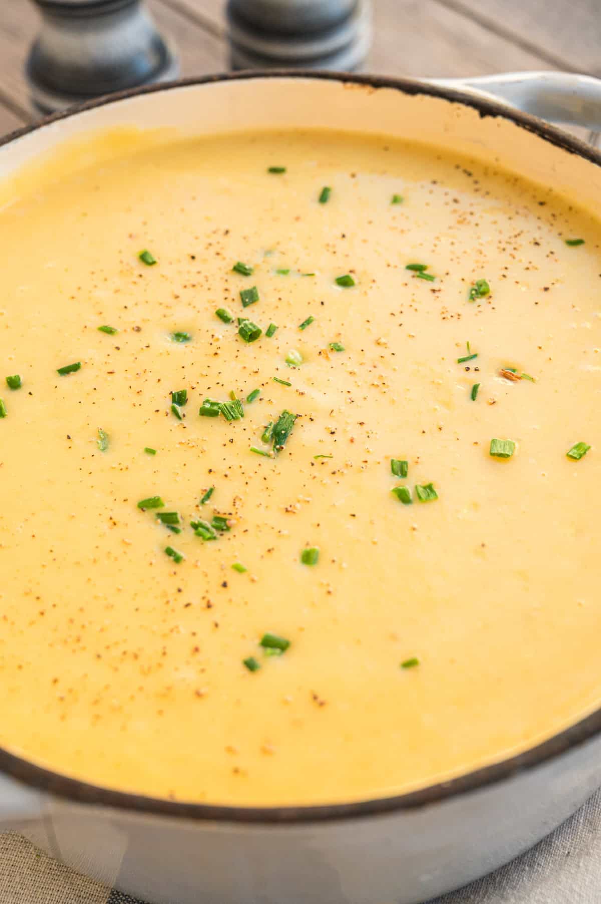 Kartoffelsuppe mit Schnittlauch in hellgrauem Topf von oben, Nahaufnahme