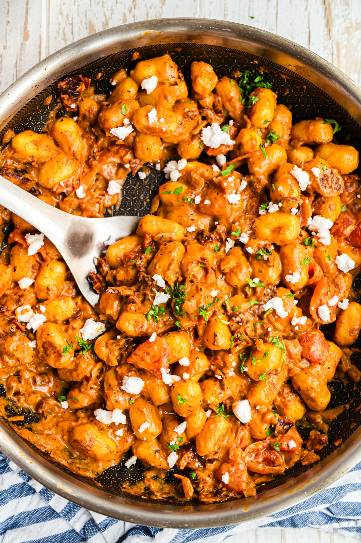 Gnocchi in cremiger Tomatensauce in Pfanne mit Feta und Petersilie, von oben, Nahaufnahme
