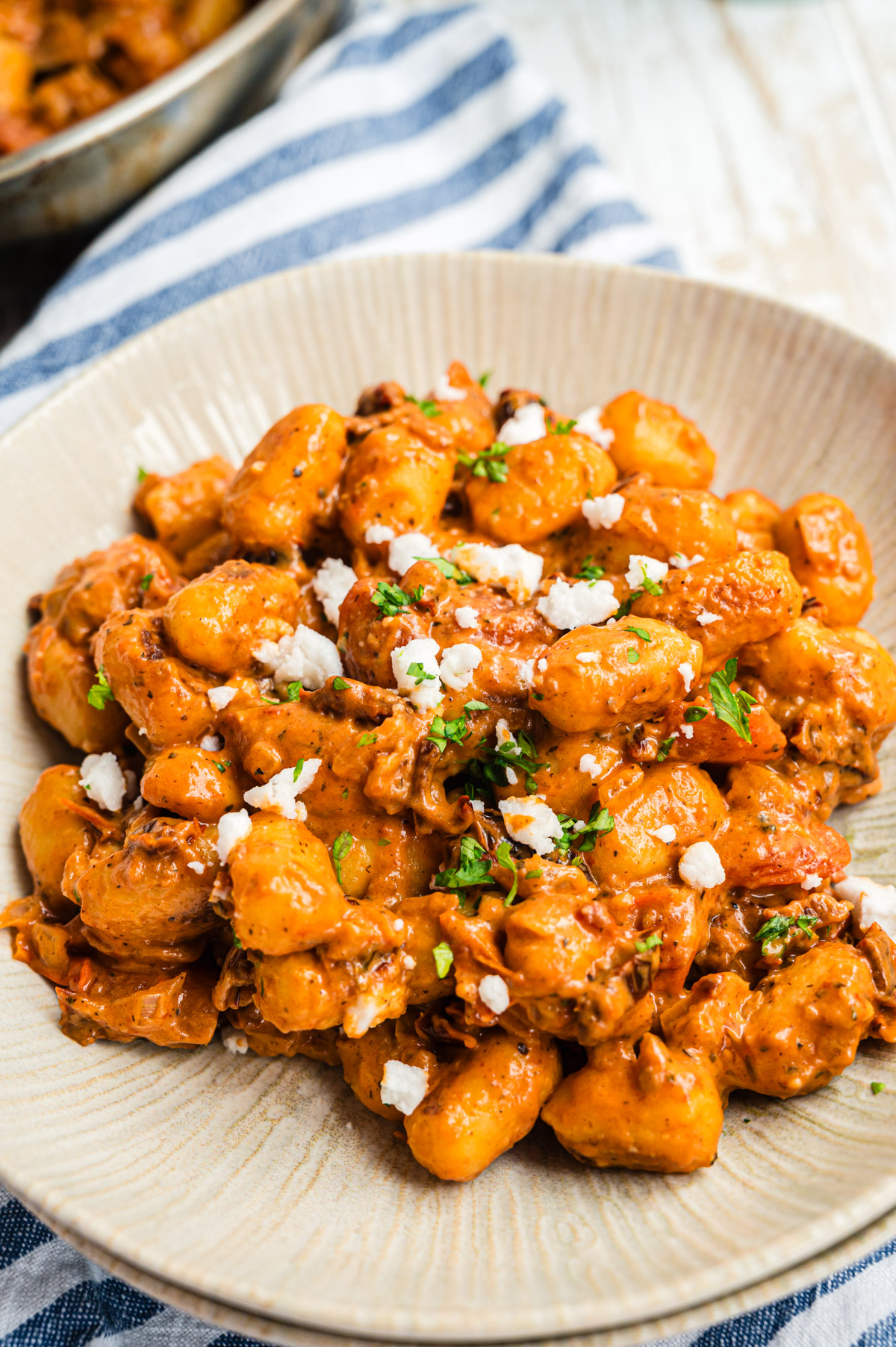 Gnocchi in cremiger Tomatensauce in heller Schale mit Feta und Petersilie, Nahaufnahme