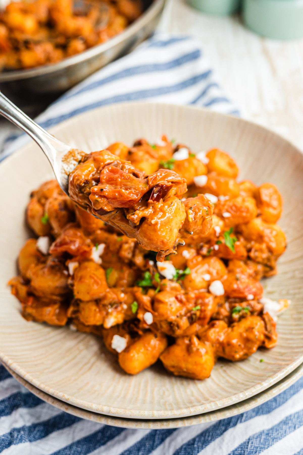 Gnocchi in cremiger Tomatensauce in heller Schale. Portion auf Gabel wird hochgehalten