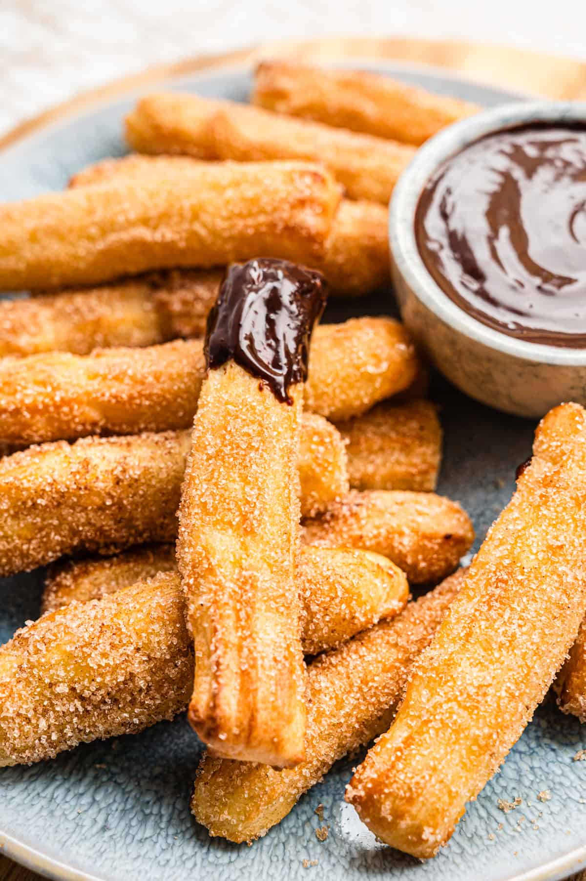 Airfryer Churros auf blauem Teller mit Schokoladensauce, einer wurde reingetaucht