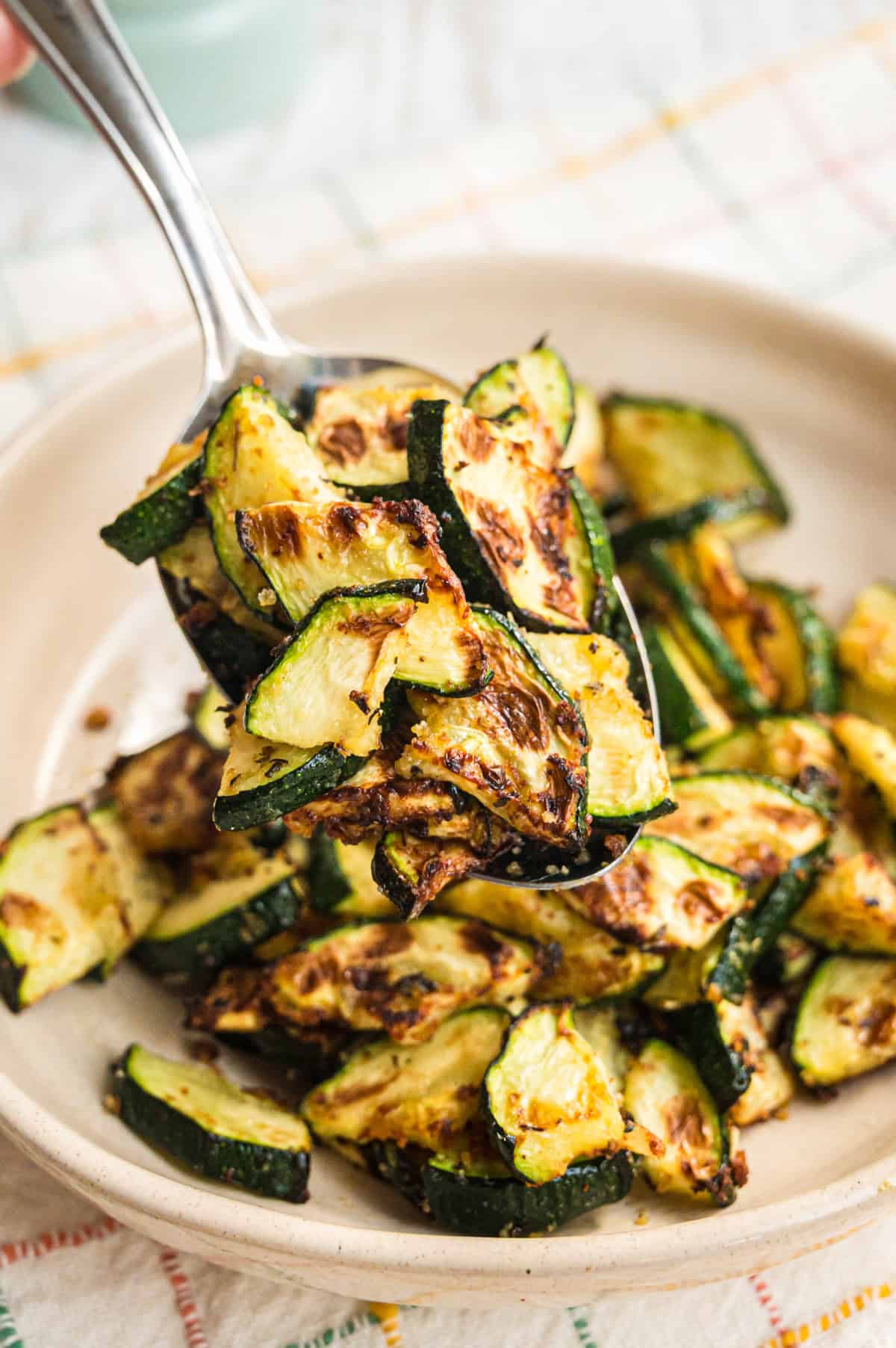 gebackene Zucchini auf Löffel über Schüssel mit mehr Zucchini