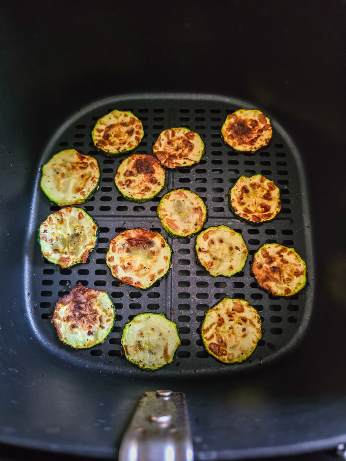 gebackene Zucchinischeiben in einer Lage im Korb des Airfryers