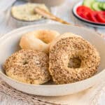 4 Bagel aus dem Airfryer in einer hellbeigen Schüssel mit Frühstück-Zutaten im Hintergrund