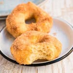 zwei Donuts mit Zimt-Zucker auf weißem Teller, einer angebissen