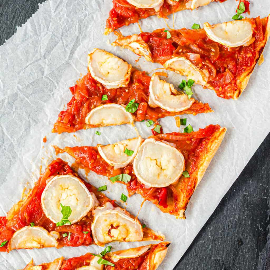Blätterteigtarte mit Tomaten und Ziegenkäse auf weißem Papier von oben