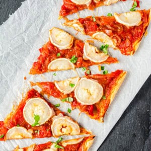 Blätterteigtarte mit Tomaten und Ziegenkäse auf weißem Papier von oben