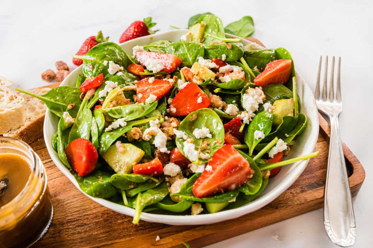 Spinatsalat mit Erdbeeren und Feta in heller Schale auf Holzbrett