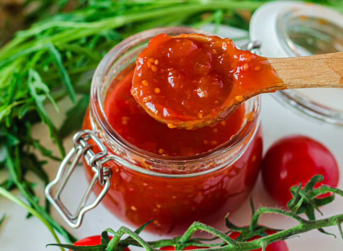 kleines Glas mit Tomaten-Chili-Konfitüre, Konfitüre auf Holzlöffel