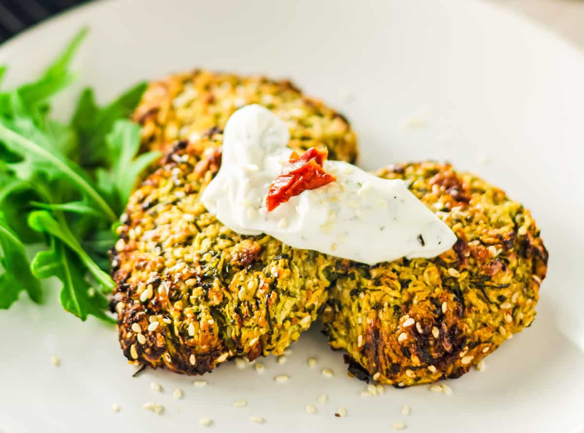Drei Zucchinipuffer mit einem Klecks Kräuterquark auf einem weißen Teller